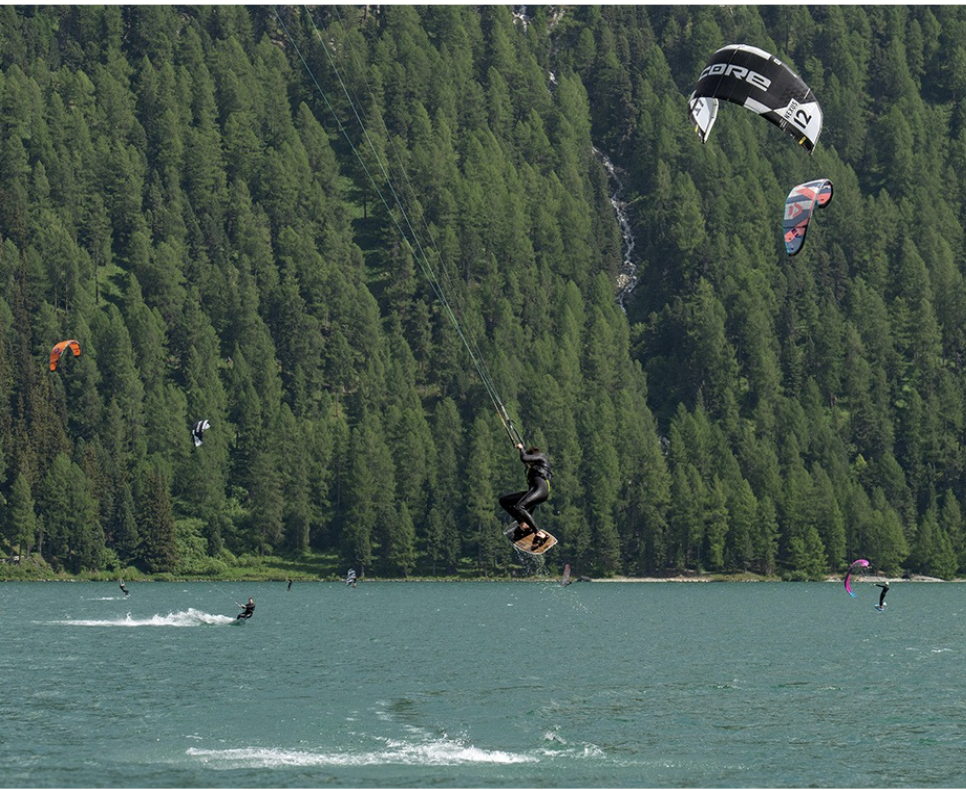 Kitesurfer springt hoch über einem Alpensee vor bewaldeten Bergen