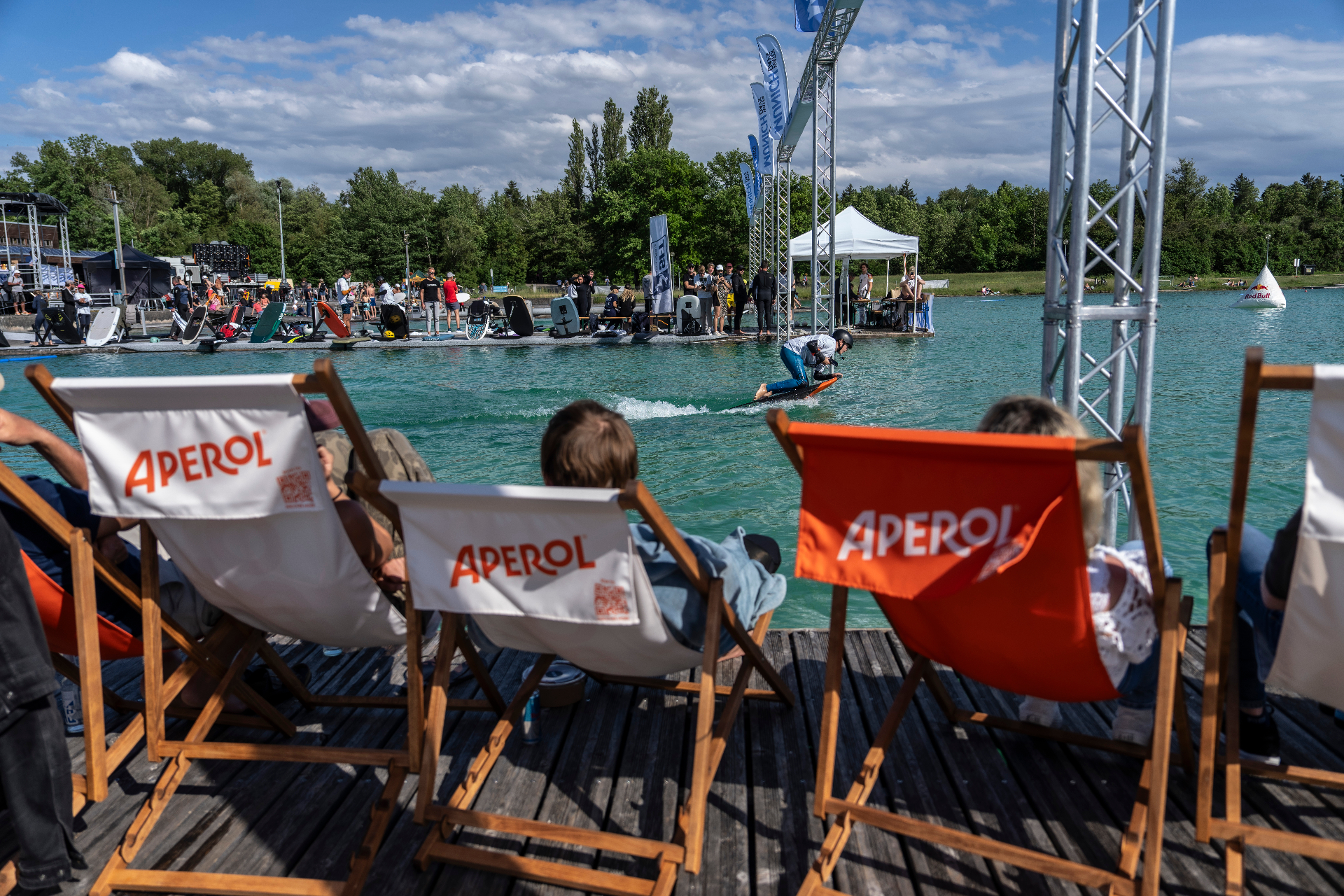 Zuschauer in Aperol-Liegestühlen verfolgen einen Skimboarder auf dem Wasser